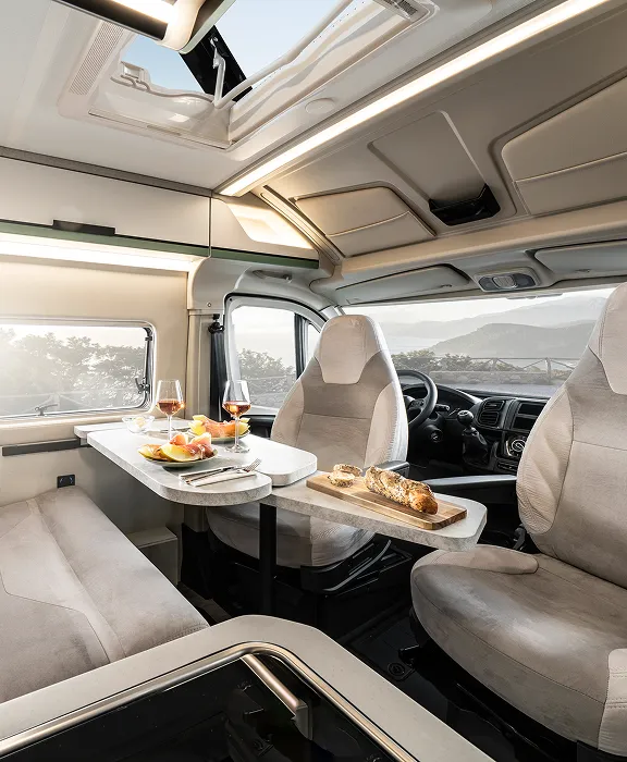 Helle Sitzgruppe im Camper mit gedecktem Tisch, Drehsitzen und Panoramablick durch das Fenster.